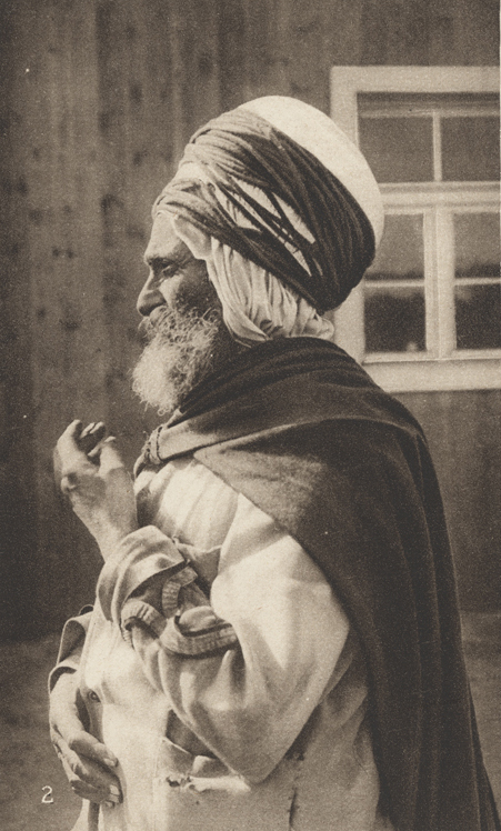 Sepia photograph of a bearded man wearing loose robes, a cloak and turban