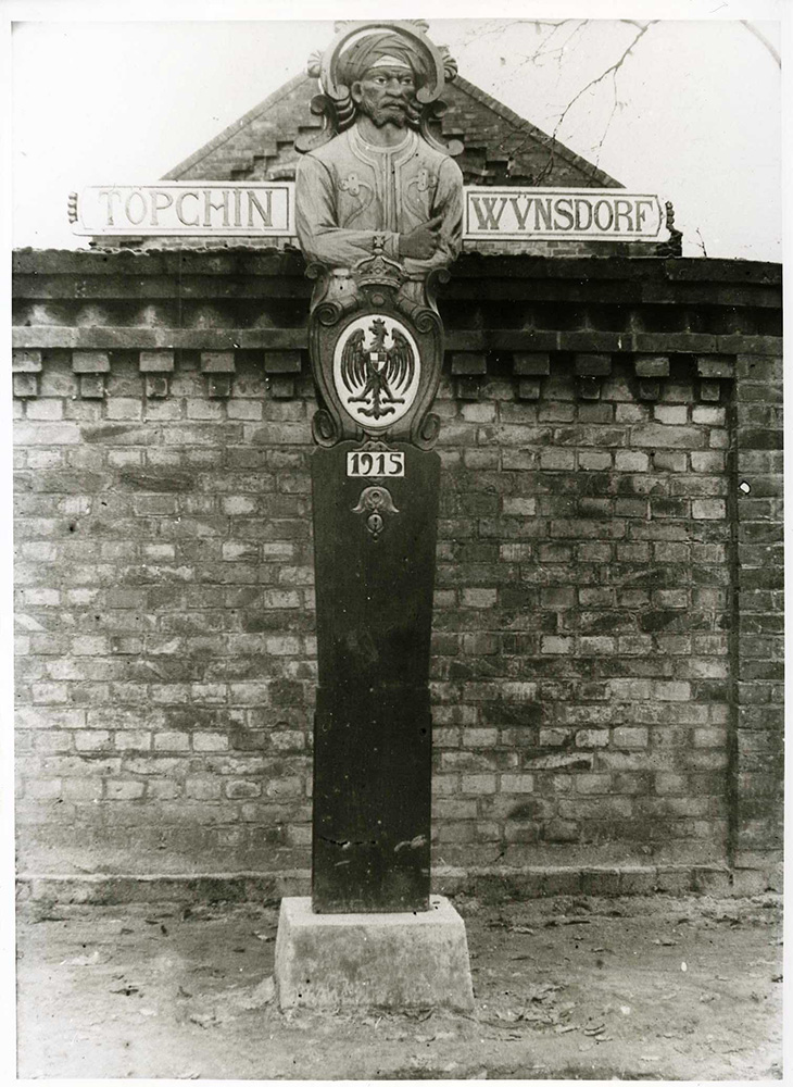 Black and white photo of a signpost with a stylized figure carved into the post