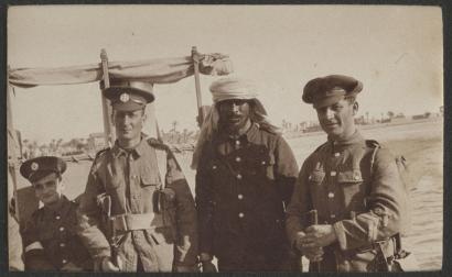 Sepia photograph of three white men in British military uniform standing on either side of a brown-skinned man wearing a military uniform with a head wrapping