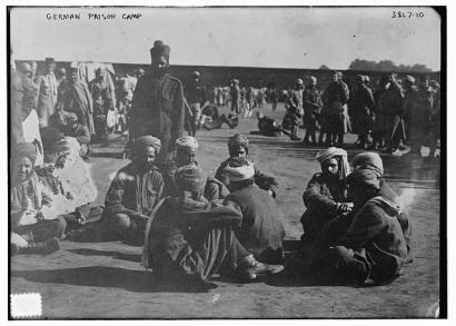 Black and white photograph of darker-skinned men dressed in loose clothing and turbans sitting and standing in groups in an open area.