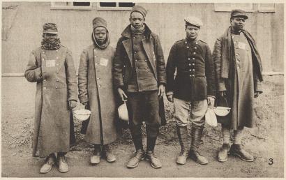 Sepia photograph of a group of dark-skinned men wearing heavy coats, standing in a row, looking at the viewer.