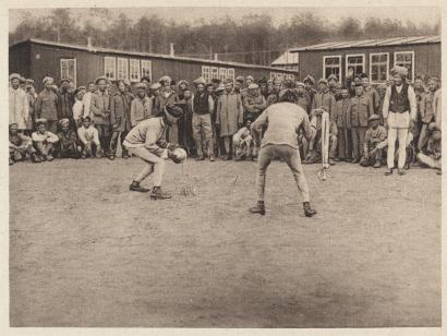 Sepia photograph of two men dressed in light form-fitting clothes handling a ball and coil of rope in front of onlookers
