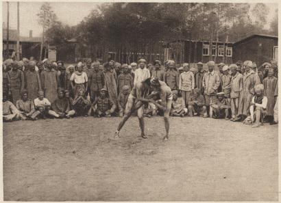 Sepia photograph of two men in stripped down to underclothes grappling with each other in front of onlookers