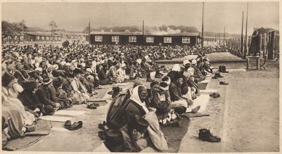Sepia photograph of rows of men kneeling on prayer mats in an open area